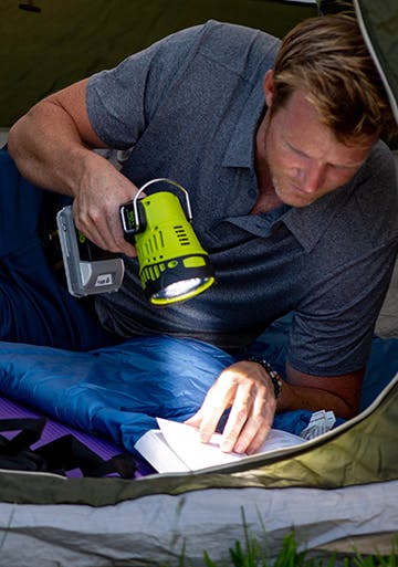 Man using the 24-Volt Cordless Handheld Flashlight to read a book in a tent.